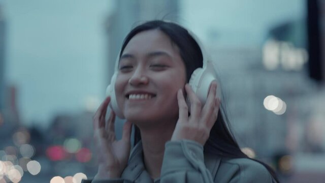 Happy japanese woman listening music in headphones outdoors
