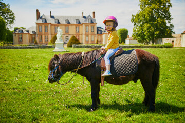 Adorable three years old girl riding a pony