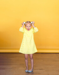 Beautiful girl in a yellow dress on a solid yellow background. Blonde with long hair. Emotions.	