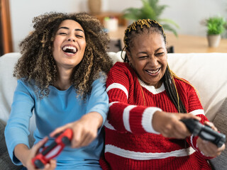 Happy African mother and daughter having fun playing online video games at home - Gaming...