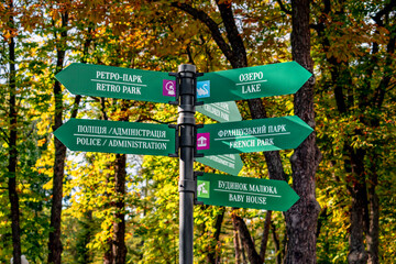 Kharkiv, Ukraine - October 20, 2020: A pillar with direction signs in Gorky Park in Kharkov. Many green arrows on a metal column against the background of yellow-orange leaves of an autumn garden