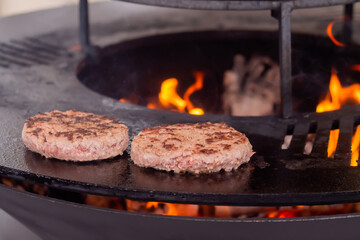 Process of grilling fresh meat cutlets for burgers on brazier with hot flame at summer local food market - close up view. Outdoor cooking, gastronomy, cookery, street food concept
