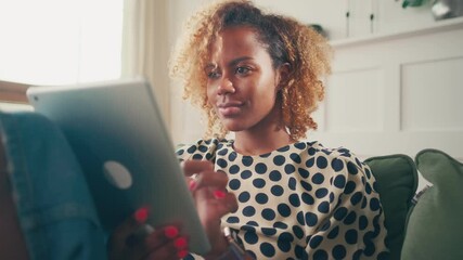 Satisfied african american woman with digital tablet resting at home on sofa. Happy young woman browsing social networks, chatting, shopping online or using apps. Concept of modern electronic devices. - Powered by Adobe