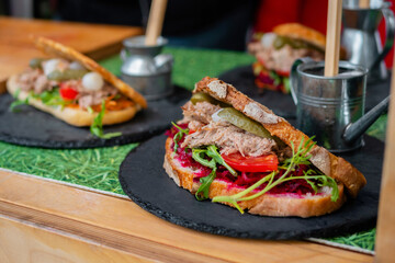 Sandwich with tuna, arugula, pickle, tomato, beetroot on counter at summer local food market - close up. Gastronomy, street food, mediterranean and Italian dish concept