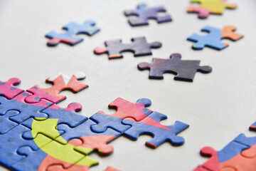 Selected focus on Fragment of a folded jigsaw puzzle and a pile of uncombed puzzle elements against the background of a white surface