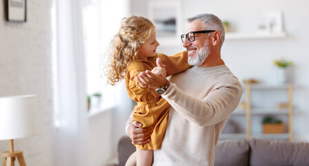 Adorable child girl and positive grandpa holding hands while dancing together in living room - 456891922