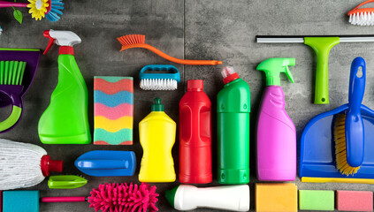 Autumn cleaning. Colorful set of bottles with clining liquids and colorful cleaning kit on gray tiles.