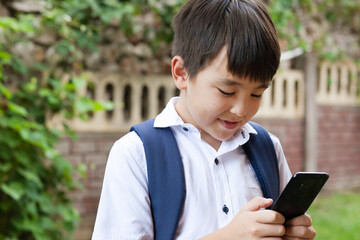 
Cute asian schoolboy boy writes a message on the phone outdoors. Communication and gadgets