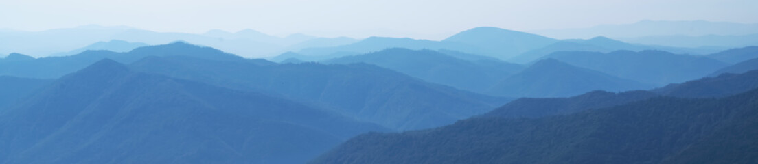 Panorama of dark blue mountain landscape in fog. Horizontal image. Selective focus.
