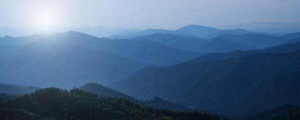 Panorama of dark blue mountain landscape in fog. Horizontal image.