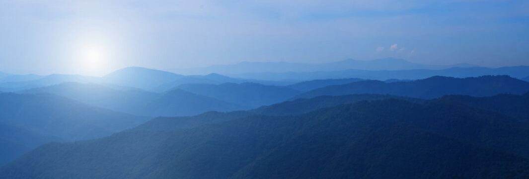 Panorama of beautiful dark blue mountain landscape in fog. Horizontal image.