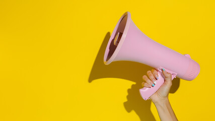 A woman's hand holding a pink megaphone isolated on a yellow background. Creative announcement...