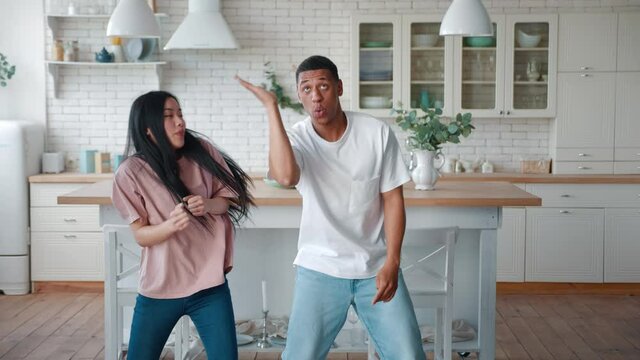 Beautiful romantic interracial heterosexual couple of Asian woman girlfriend and African american guy boyfriend dancing in the modern kitchen at home, beautiful people enjoying their day off together