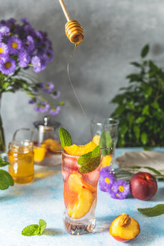 Woman hand perfused honey on peach infused water, cocktail, lemonade or tea. Summer iced cold drink with peach and mint on light gray table surface