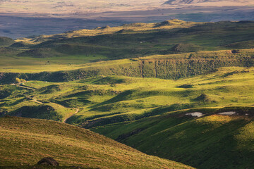 Obraz premium A view from afar of a rugged terrain with green pastures on the hills illuminated by the setting sun