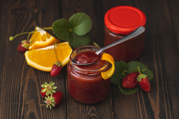 Homemade strawberry jam or marmalade with orange in the glass jar and ripe strawberries on the wooden table