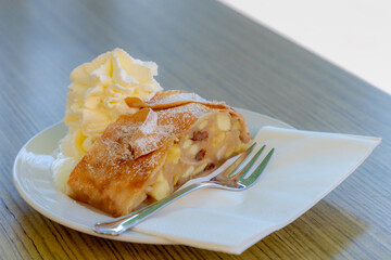 Selective focus of Apfelstrudel (Apple Strudel) served delicious icing sugar and white whipping cream on wooden table, A classic Viennese apple dessert, Vienna, Austria.