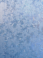 Winter light white and blue background or wallpaper. Drawing of crystals of ice and frost on the window pane. Abstract Christmas and New Year vertical backdrop