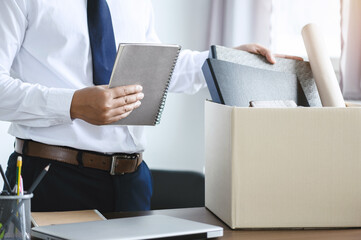 personnel packing personal belongings and files into a brown cardboard box with resignation letter for changing and resign from work concept for quit or change of job - obrazy, fototapety, plakaty