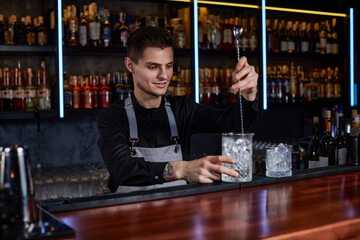 Barman stirring ice cubes in cocktail glass with spoon