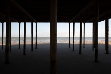 view of a sunny sea from under a pier standing on wooden poles