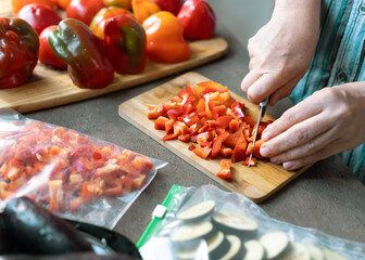 A woman cuts red peppers and eggplants into pieces and puts them in plastic freezer bags. Freezing vegetable.