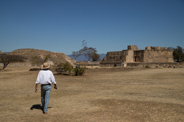 A man in a hat walks through an ancient city in Mexico. 