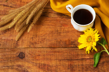 Obraz na płótnie Canvas autumn tea cup composition, yellow scarf, spikelets of wheat and sunflower flower on a wooden background