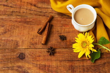autumn tea cup composition with milk, yellow scarfs, cinnamon sticks and sunflower on a wooden background