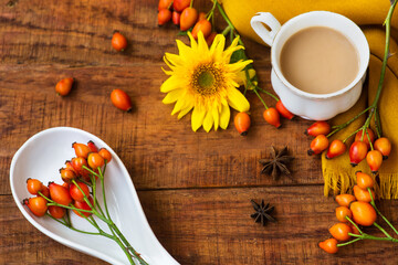 autumn tea cup composition with milk, yellow scarfs, sunflower and rosehip on a wooden background