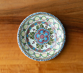 Colorful folk art ceramic wall plate on a wooden board