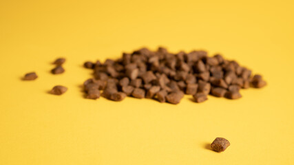 Small and big heaps of cat food. Big and small food portions. Pet food on yellow background. Stack of dog food