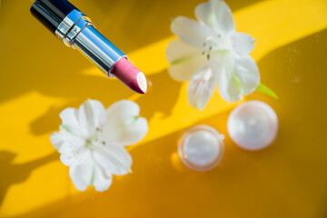 composition with lipstick and flowers on yellow background. Creative flat lay of pink Lipsticks and white alstroemeria frozen in the air. Romantic, beauty concept.decorative makeup products