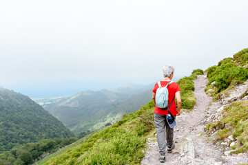 senior woman hiker with backpack and gray hair walking on a mountain path