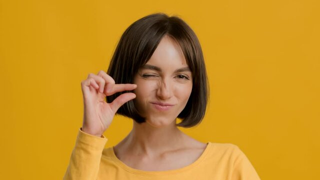 Female Gesturing Small Size With Fingers Posing Over Yellow Background