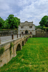 Fototapeta premium Parma, Italy: Entrance-fortress of Cittadella park, a bridge over the meadow, and its visitors on sunny day