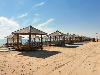 View of empty sandy beach with empty sun beds under awnings. Red flag warning about the ban on swim