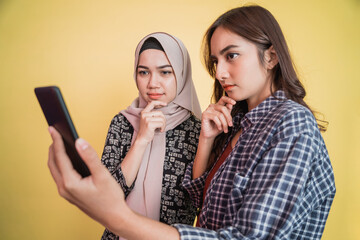 a woman in a headscarf and a woman with long hair looking at the screen of a mobile phone seriously...