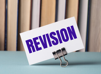 A white card with the text REVISION stands on a clip for papers on the table against the background...