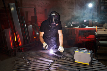 a welder in a helmet and gloves in a workshop works with an inverter welding machine