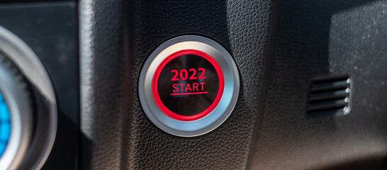 Finger press a car ignition button with 2022 START text inside modern electric automobile. New Year...
