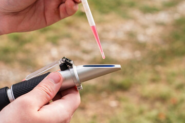 the winemaker applies a drop of grape juice with a pipette to the prism of a refractometer to determine the amount of sugar in the grape juice
