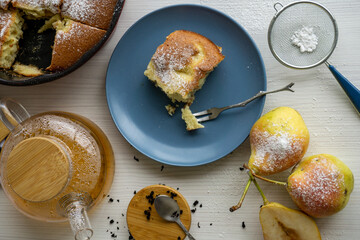 A piece of pear pie for tea on a blue plate on a white table with pears in the foreground