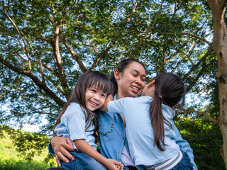 Naklejka premium Two sibling little girls with mom laughing and hugging each other on warm and sunny summer day in the garden. Young girls with her mother spending day in park.