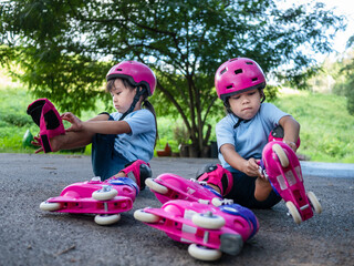 Fototapeta na wymiar Two sibling sisters wearing protection pads and safety helmet practicing to roller skate on the street in the park. Active outdoor sport for kids.