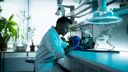 Young and Ethnic Laboratory Worker Sitting Behind a Desk Examining a Skeleton Using a Brush,...