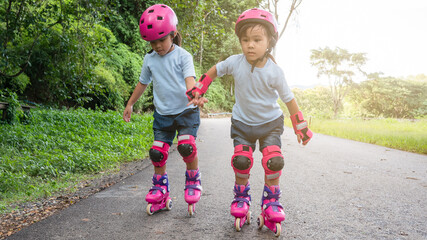 Two sibling sisters wearing protection pads and safety helmet practicing to roller skate on the...