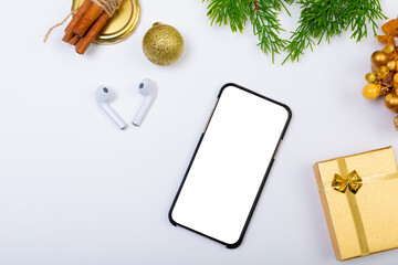 Fototapeta na wymiar Composition of smartphone with copy space, wireless earphones and christmas decorations on white
