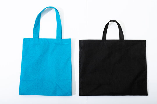 Composition of empty blue and black canvas shopping bags lying flat on white background