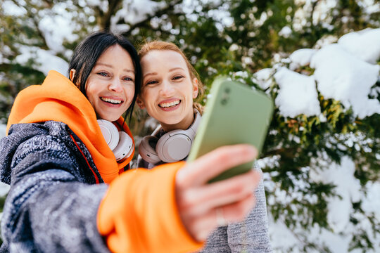 Two adult women making selfie portrait before jogging.Females runner relax after exercising, taking photographs.Two 30s brunette and blond woman posing for selfie image in winter park together.